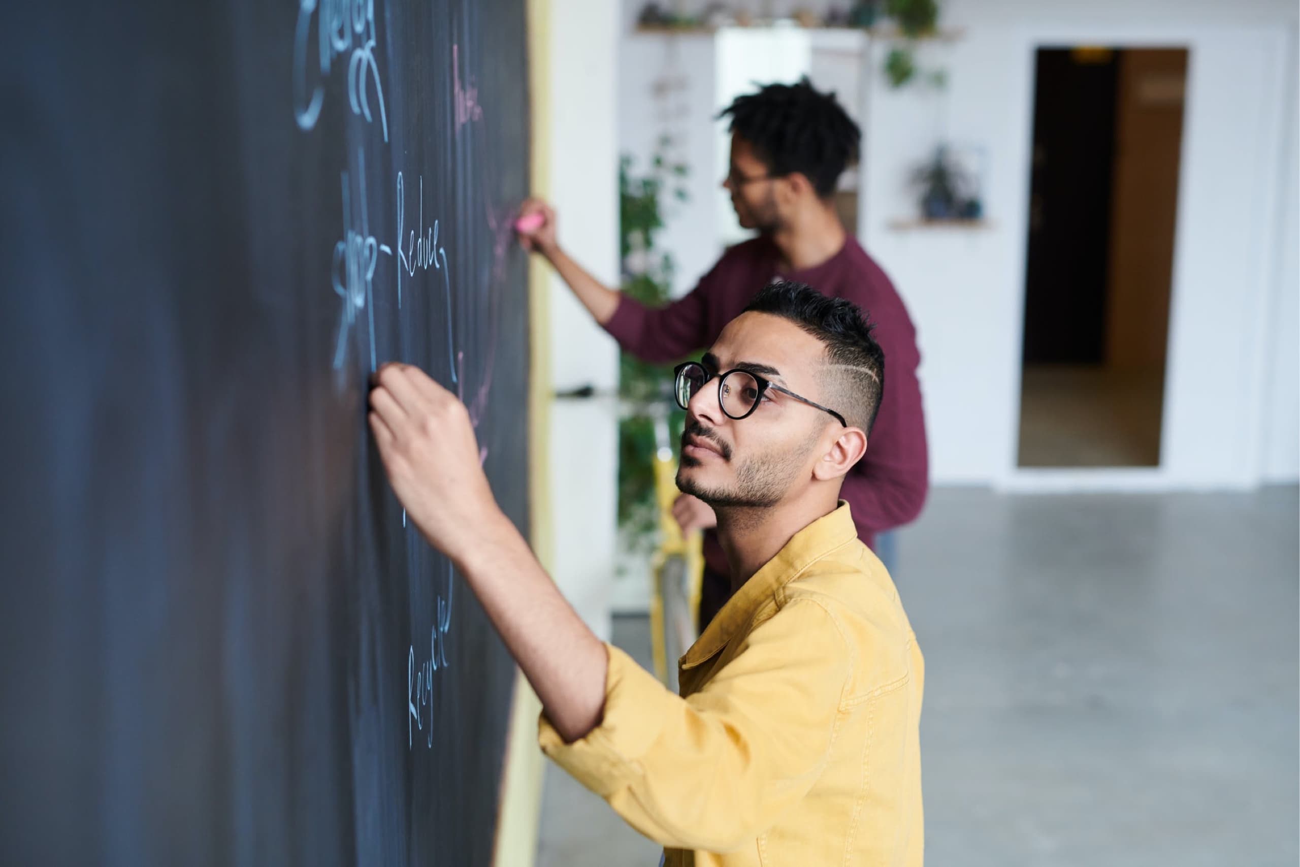 Two people writing on a black board