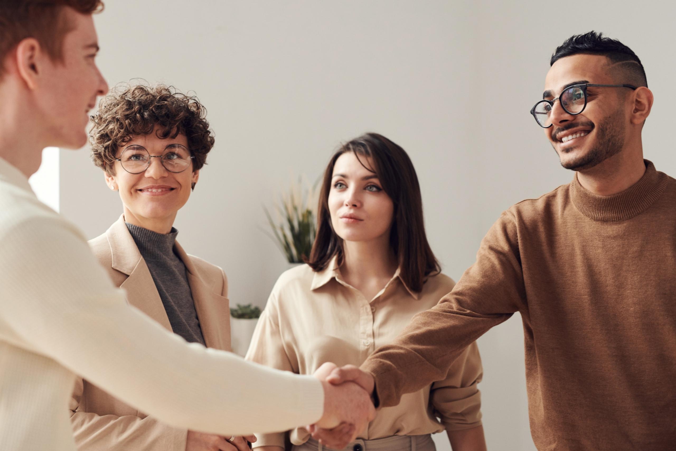 Two people shaking hands, while to team members happily observe