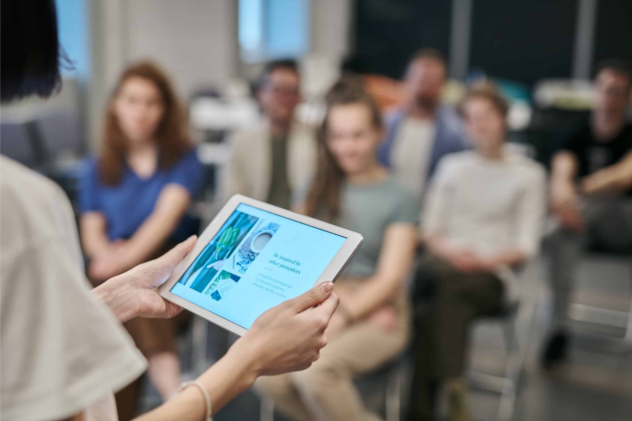 Group of people watching a person present with a tablet