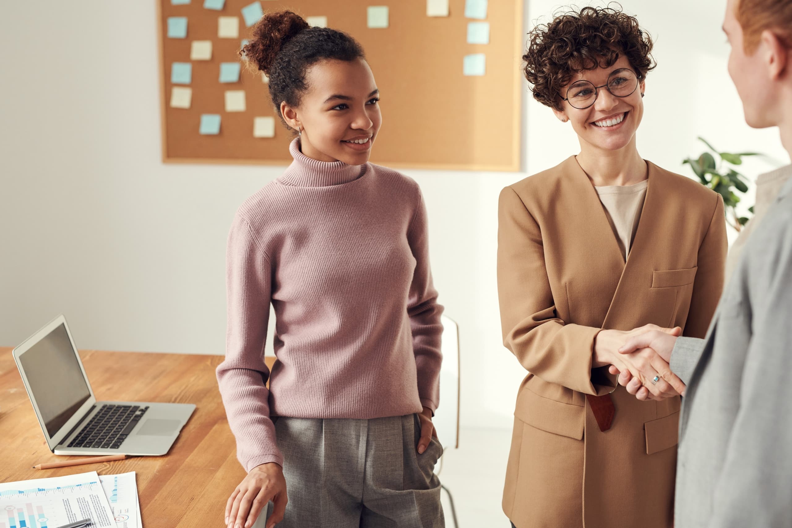 Two colleagues shaking hands while other colleague is standing next to them