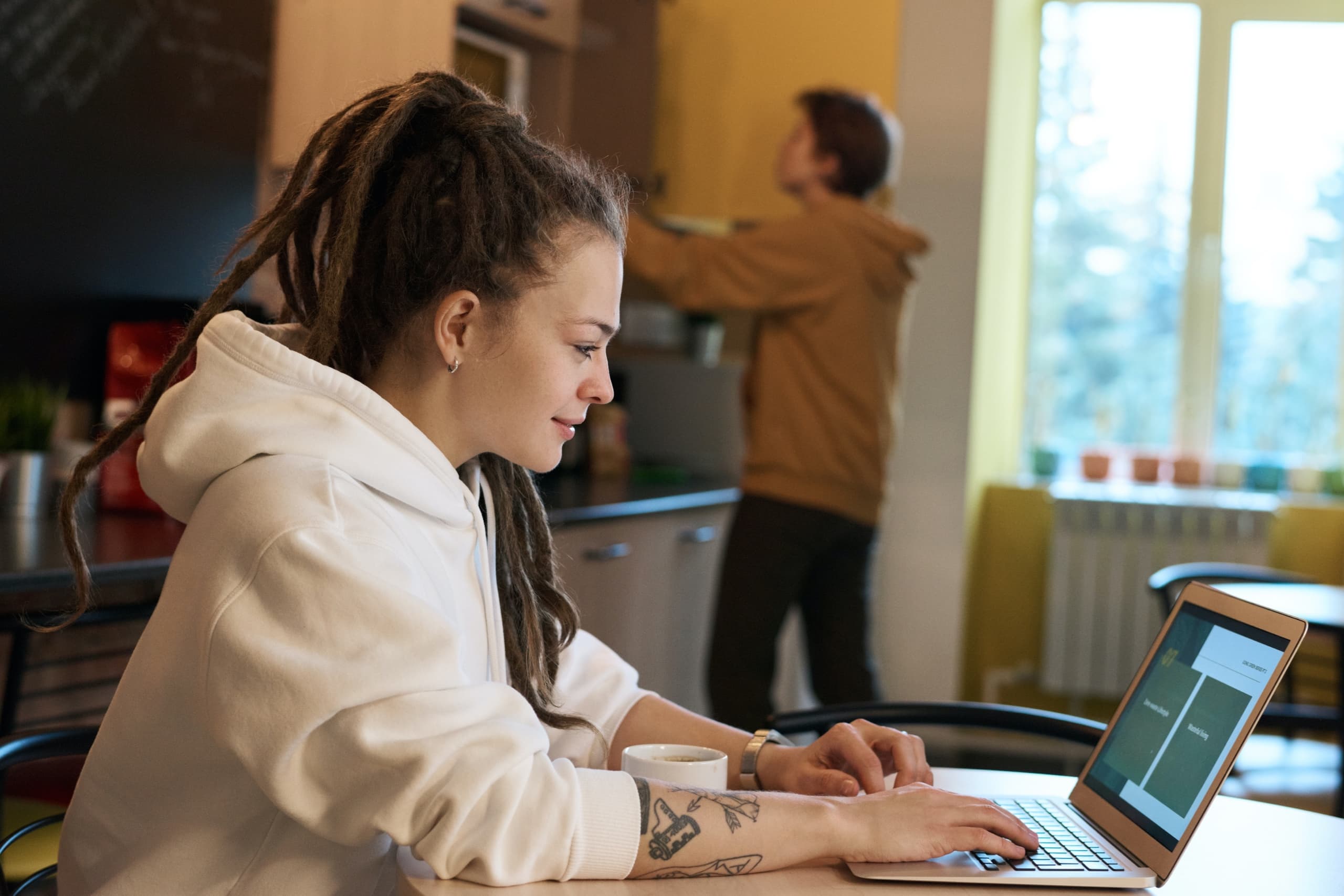 Team member working on a laptop while another team member is grabbing something from a cabinet