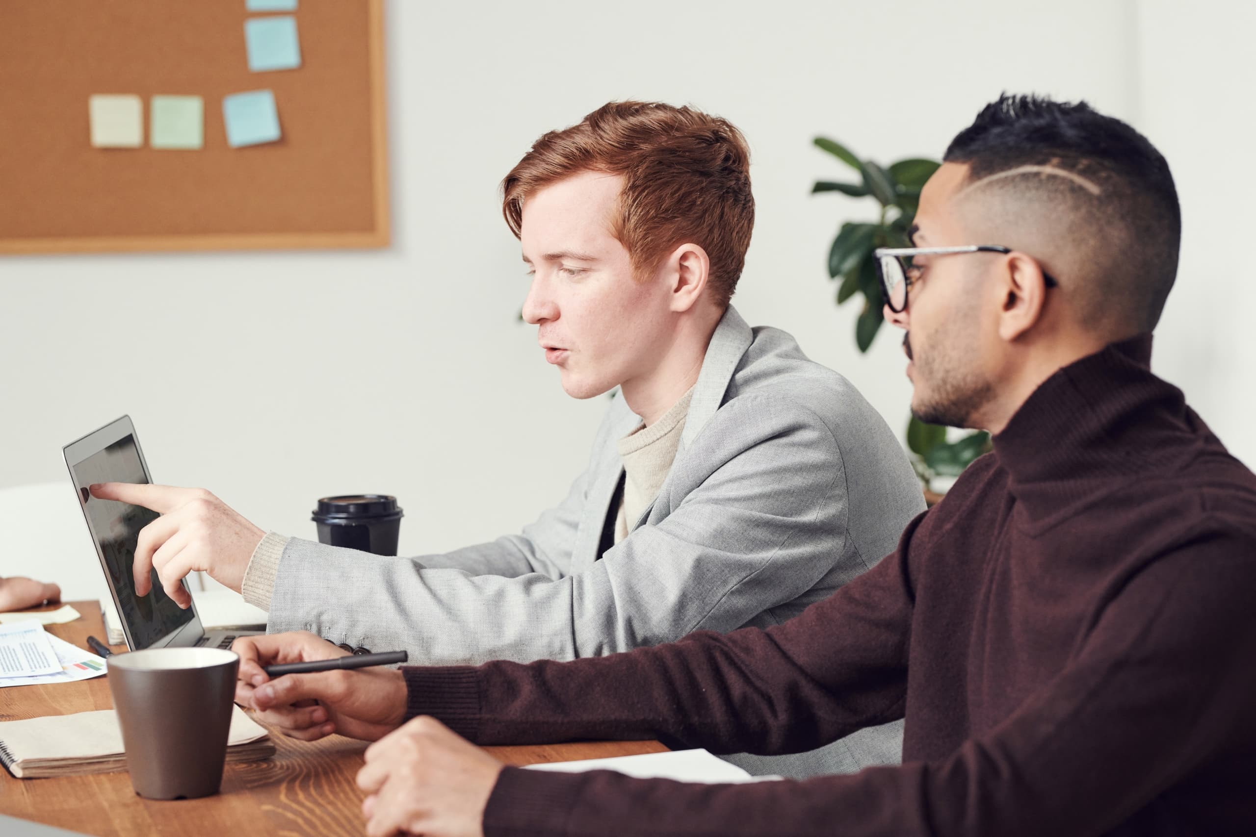 Two colleagues sitting next to each other, looking and pointing at a laptop screen