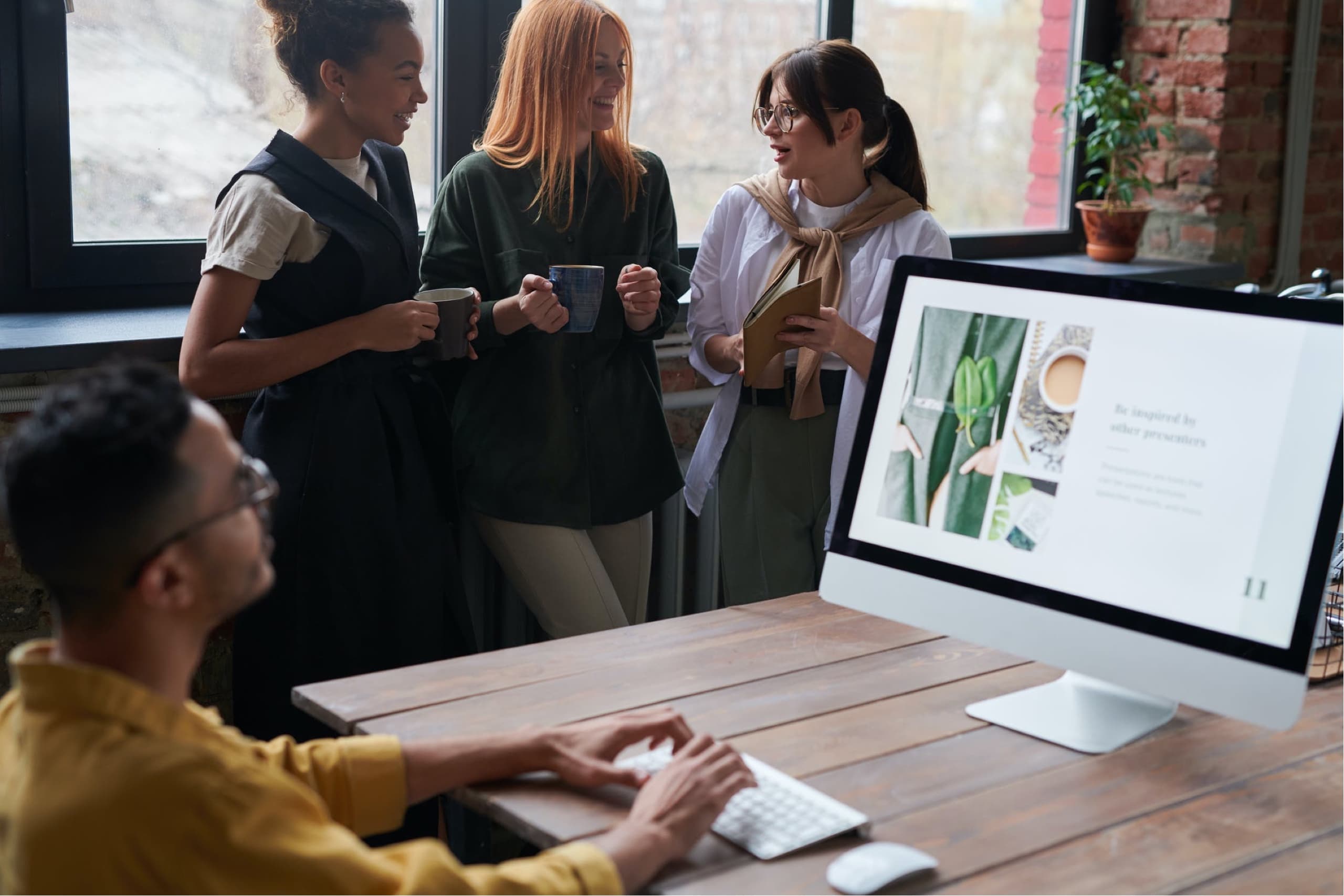 One colleague working with a imac. Three colleagues discussing in the background